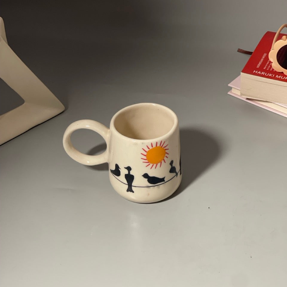 Ceramic mug with hand-painted birds on a wire and a shining sun motif
