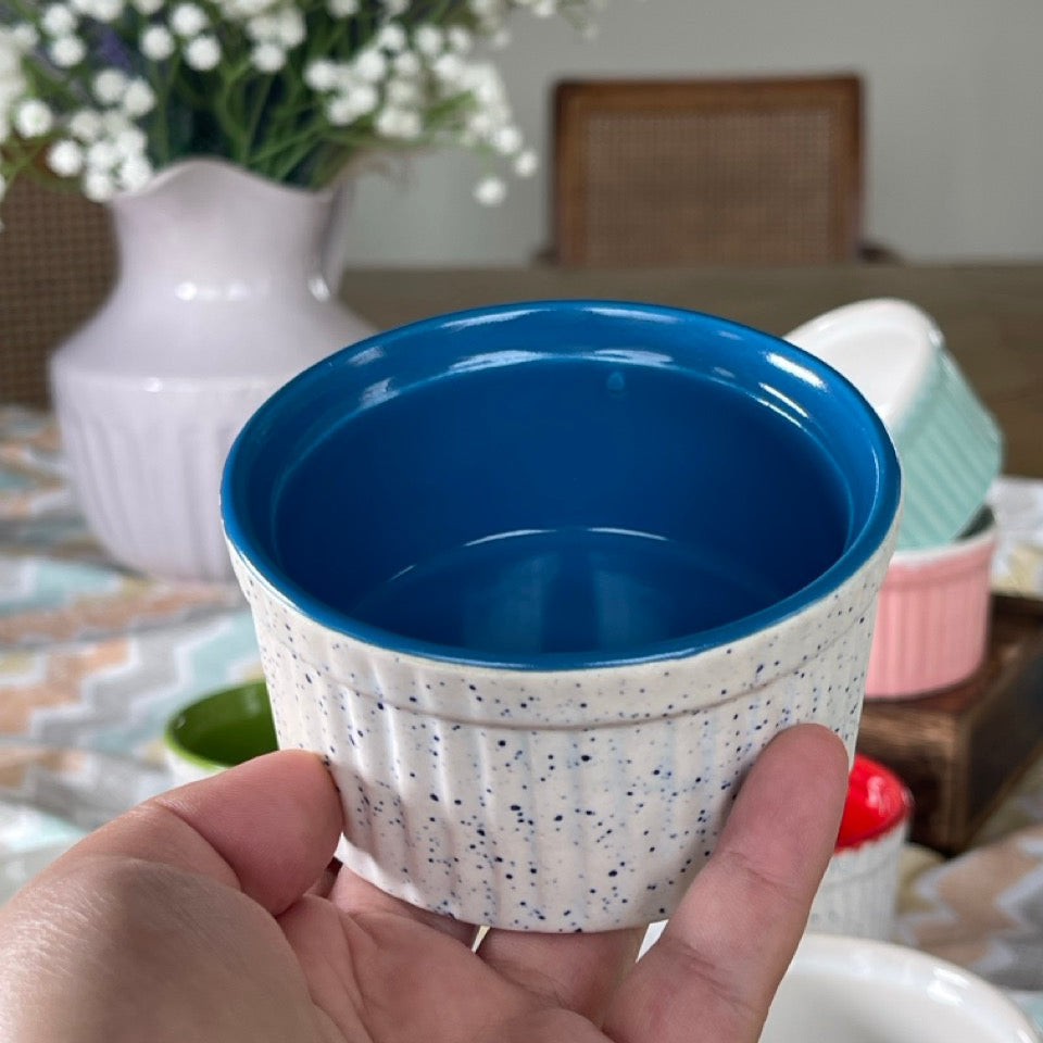 Blue ceramic cup held in a hand with a blurred background of a table and flowers.