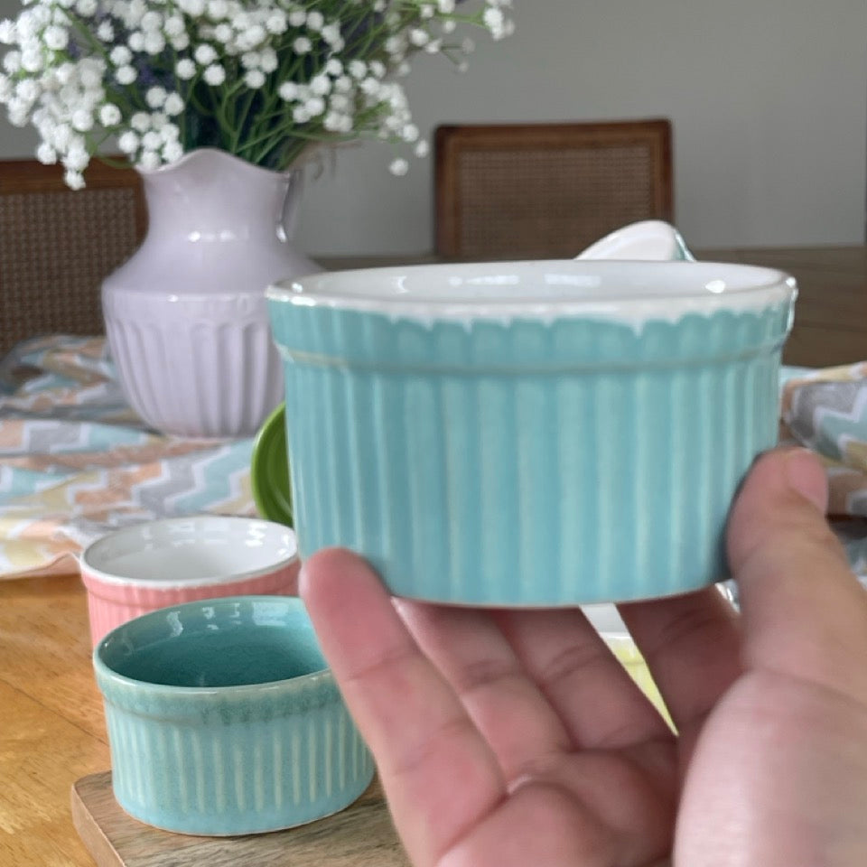 Light blue ceramic ramekin held in a hand with a blurred background of a table setting.