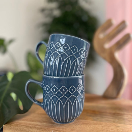 Stack of blue ceramic mugs with Kolam patterns on a wooden surface.