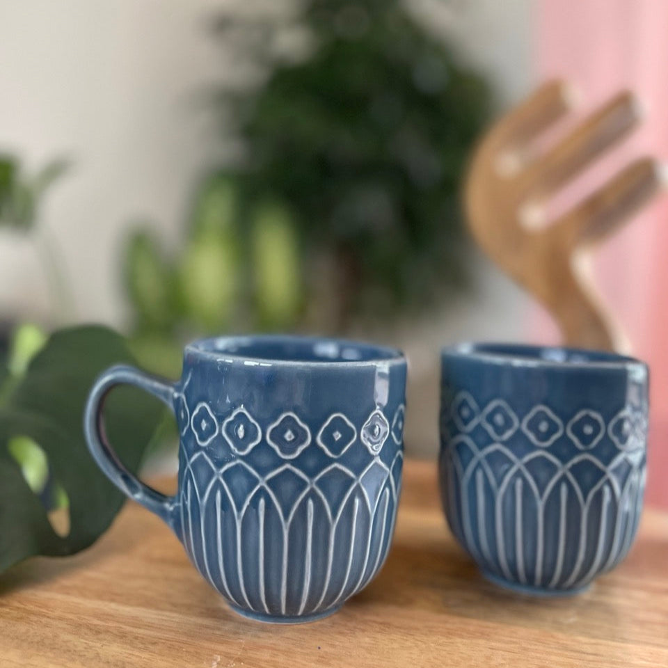 Two blue mugs with geometric Kolam inspired patterns on a wooden surface with a blurred background