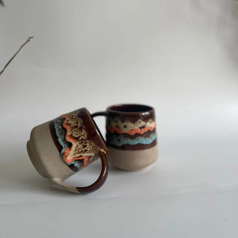Two ceramic Mountain Moods mugs with decorative handles on a plain background