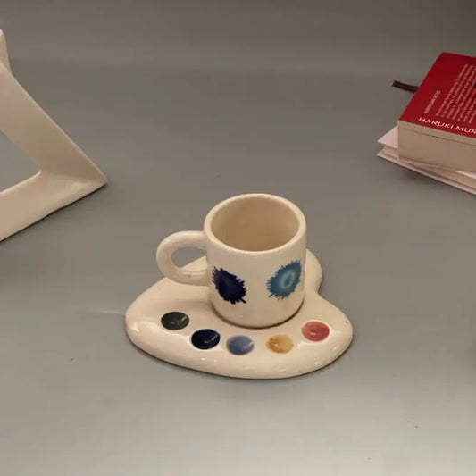 Splotch Palette shaped ceramic cups with saucer featuring artistic designs on a gray surface