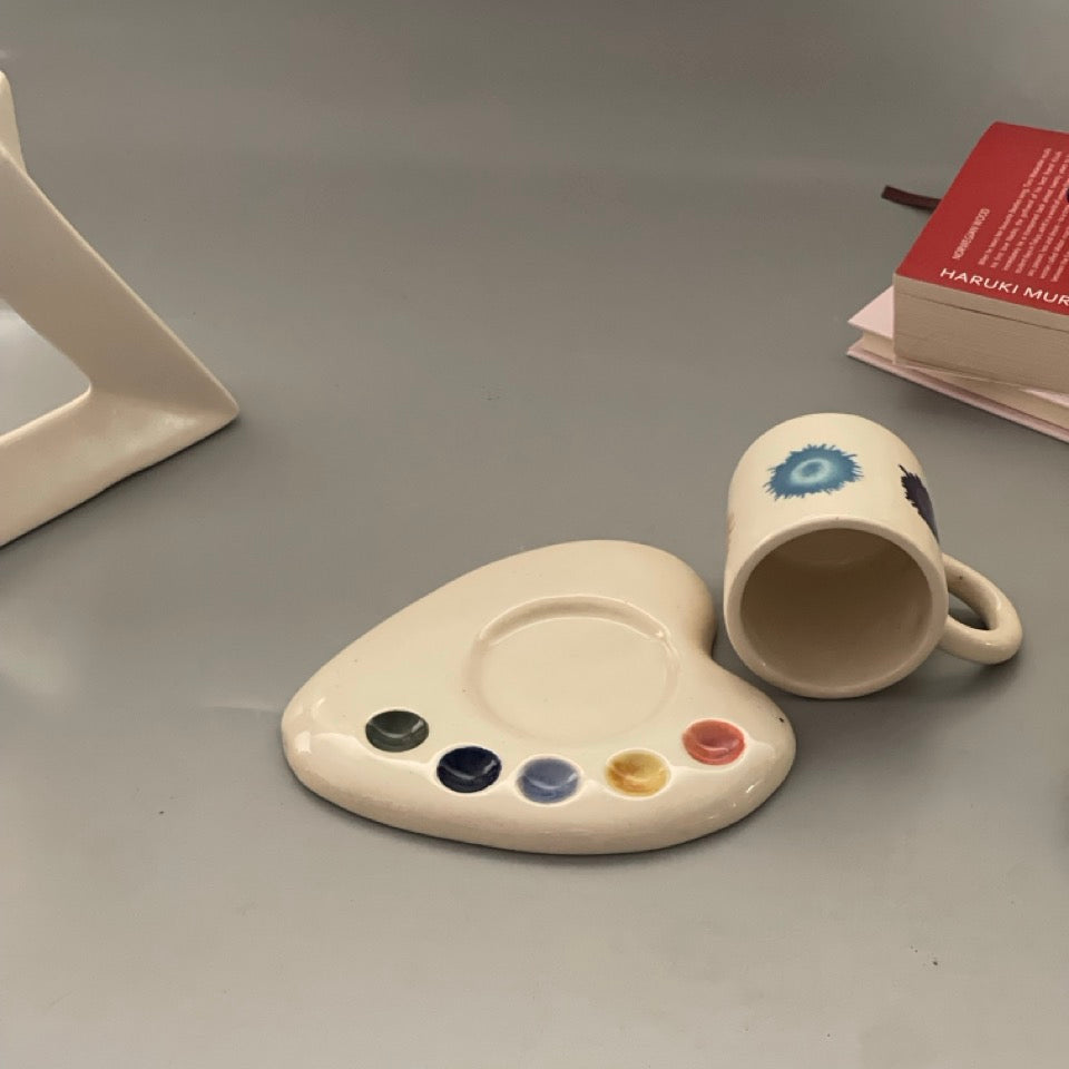 Palette-shaped ceramic cup and saucer set with artistic paint splotch and brushstroke designs