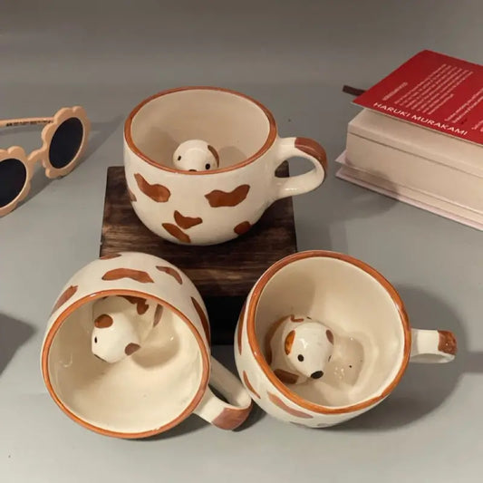 Three ceramic Paw print mug with hidden dog figurines on a gray surface, with sunglasses and a book in the background.