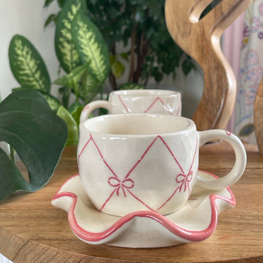 Two ceramic cups with saucers on a wooden surface with a plant in the background