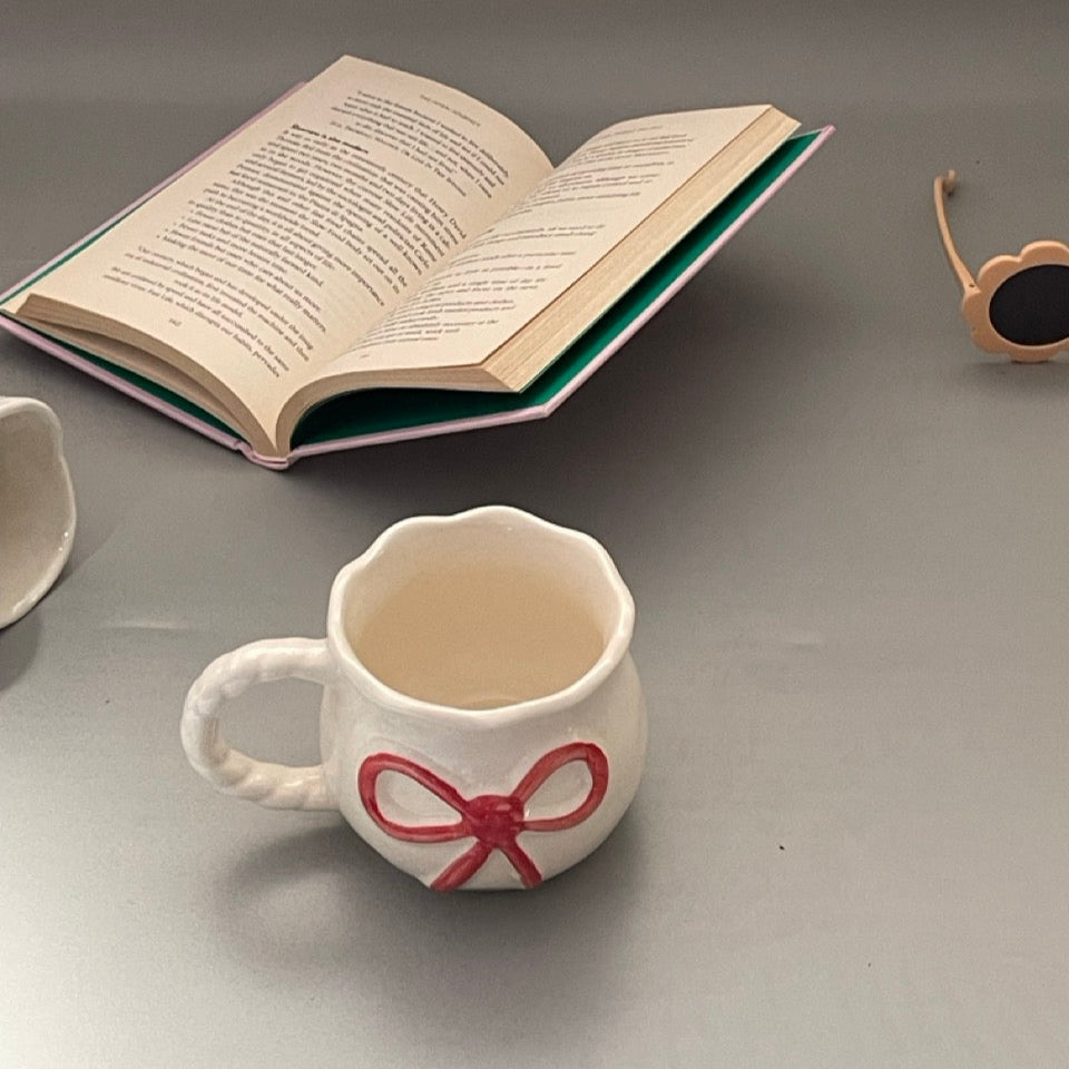 Glossy ceramic mug with bow front and sculpted handle, Pinterest-inspired design in pastel tones