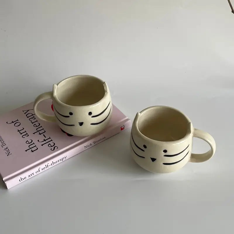 Two ceramic mugs with face designs on a book titled 'The Art of Self-Therapy'.