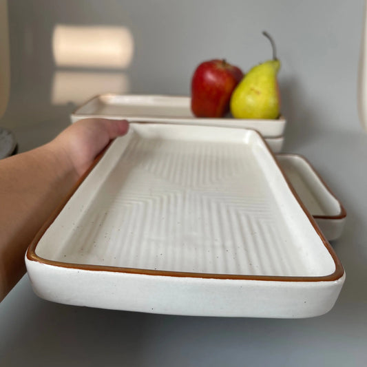 White ceramic tray with brown rim held by a hand, with fruits in the background.