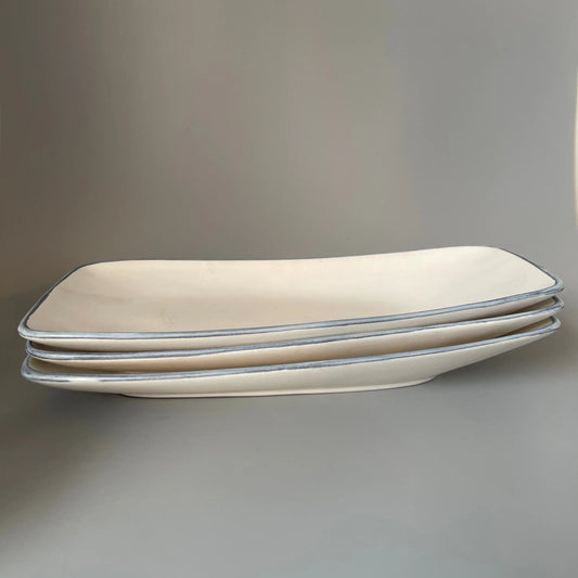 Stack of beige rectangular white with blue rims platter on a gray surface
