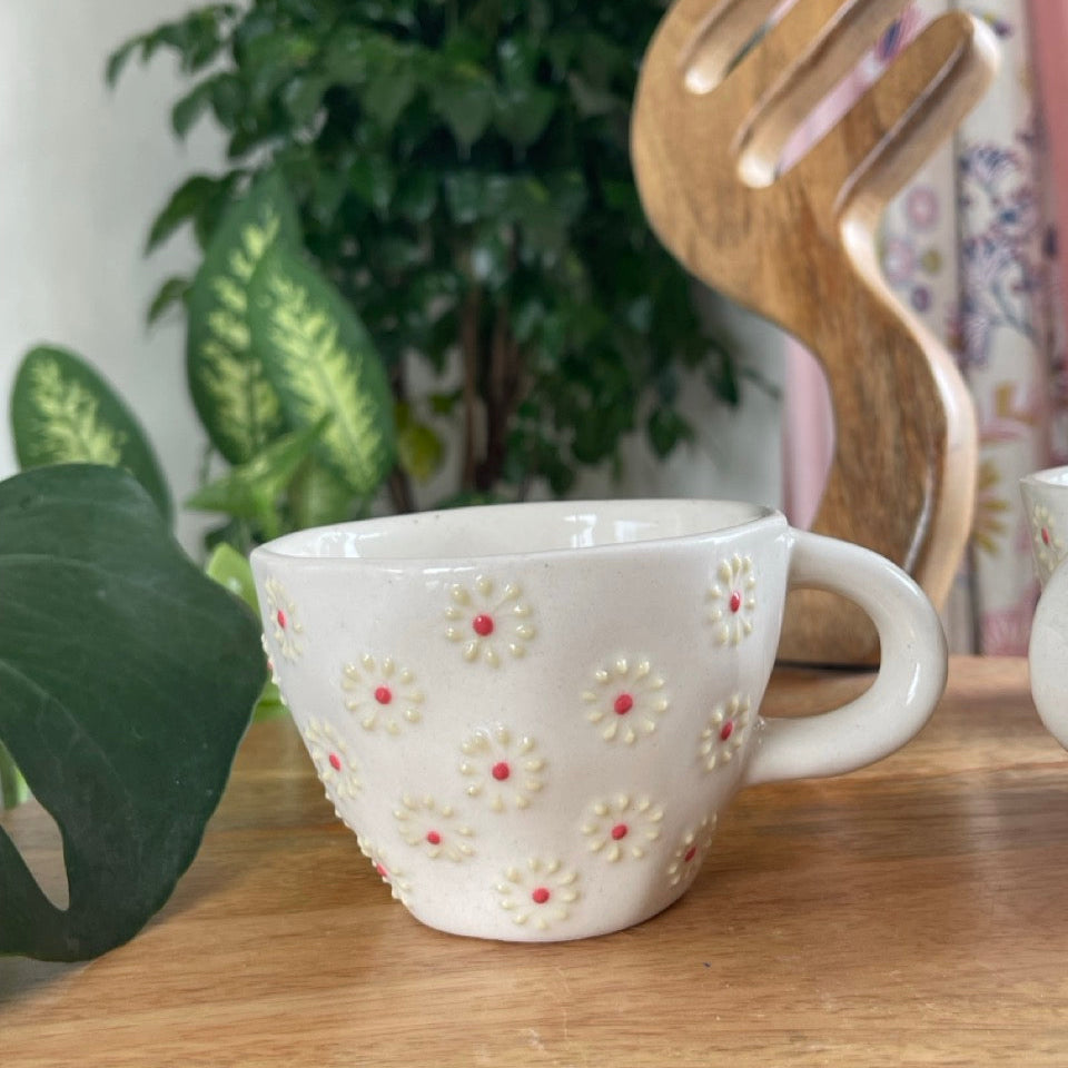White ceramic mug with floral pattern on a wooden surface with decorative items in the background.