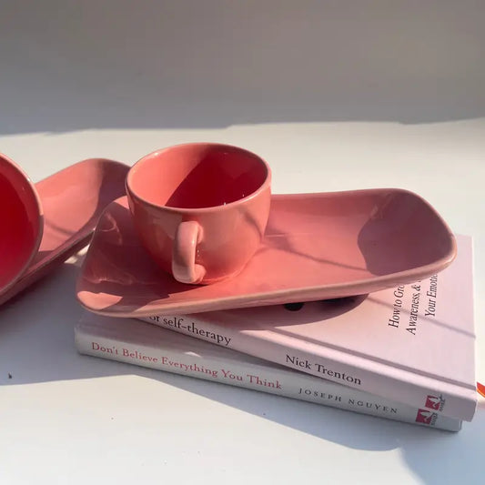 Pink Biscotti ceramic cup and saucer on a stack of books with a white background