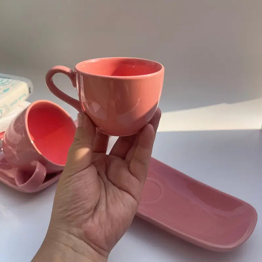 Hand holding a pink Biscotti ceramic cup with a matching saucer on a white surface