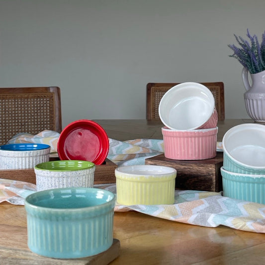 Set of colorful ceramic ramekins on a wooden table with a neutral background