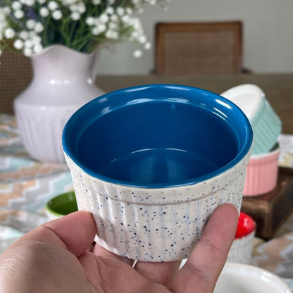 Blue ceramic cup held in a hand with a blurred background of a table and flowers.