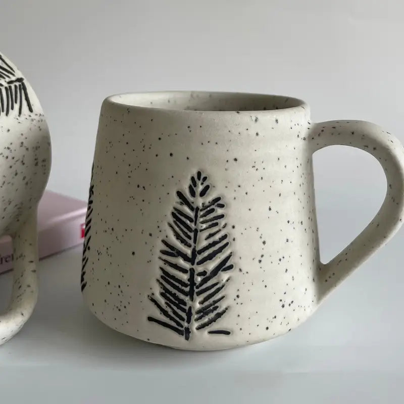 Speckled ceramic Evergreen glyph mug with black leaf design on a light gray background