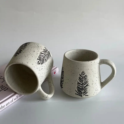 Two ceramic Evergreen glyph mugs with leaf patterns on a light gray background