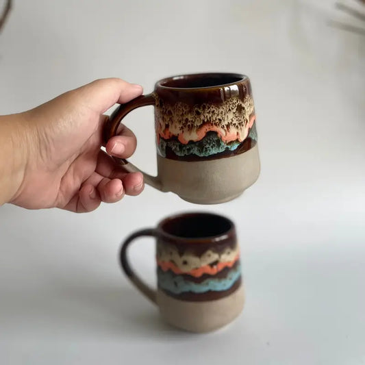 Hand holding a ceramic Mountain mood mug with a textured design on a plain background