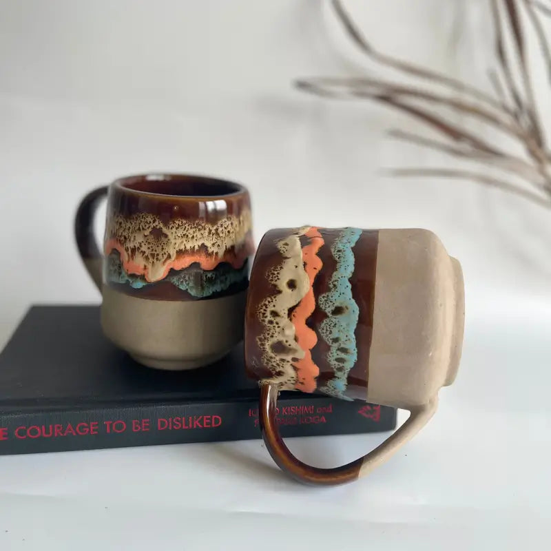 Two ceramic Mountain moods mugs with textured handles on a book against a neutral background