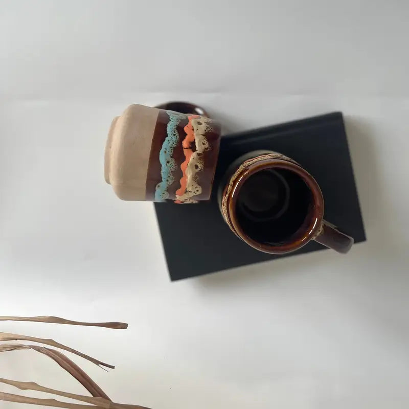 Two ceramic Mountain mood mugs on a white surface with a black square object underneath.