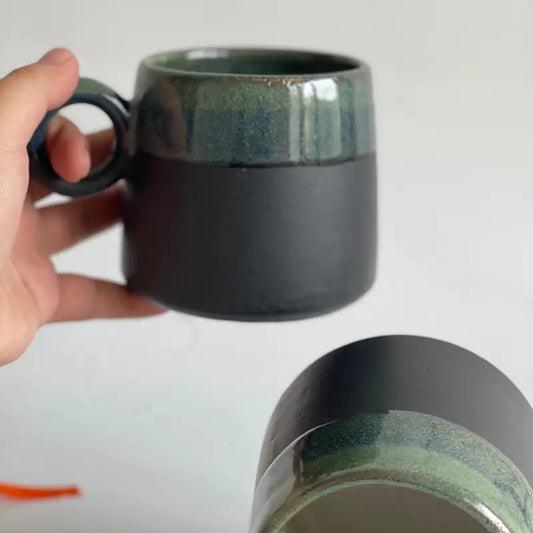 Hand holding a Orbit Handle ceramic mug with green and black glaze on a white background