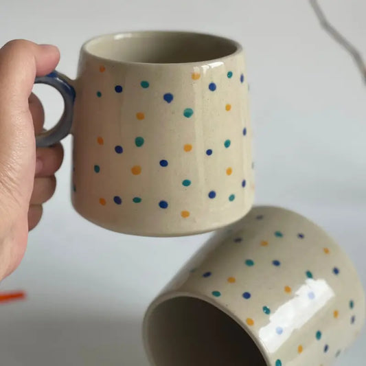 Hand holding a Orbit Handle ceramic mug with colorful polka dots on a white background