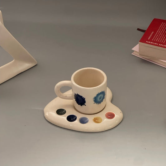 Palette-shaped ceramic cup and saucer set with artistic paint splotch and brushstroke designs