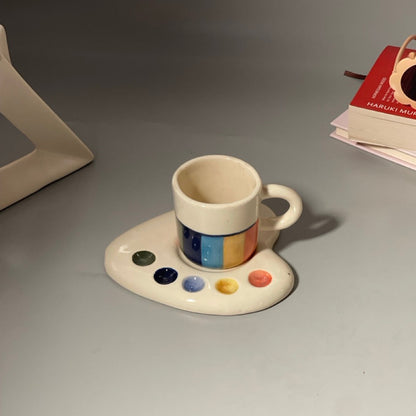 Palette-shaped ceramic cup and saucer set with artistic paint splotch and brushstroke designs