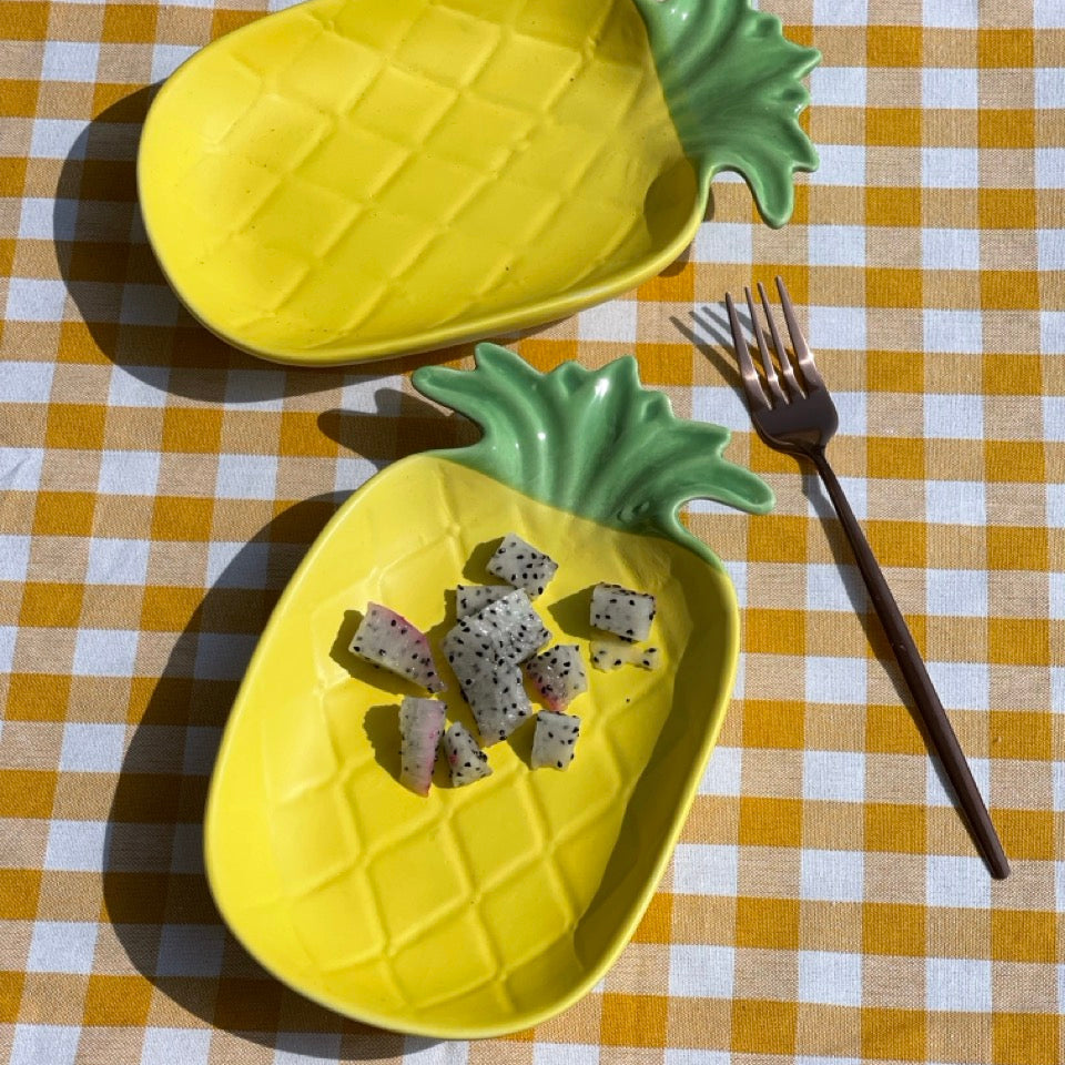 Two pineapple-shaped plates on a checkered tablecloth with a fork beside them.