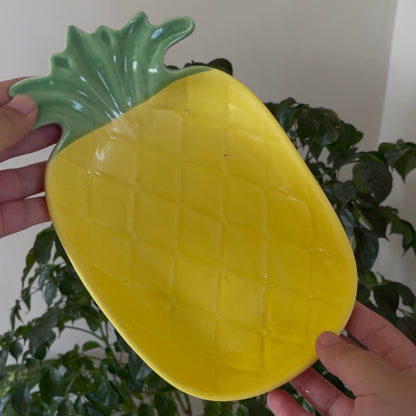 Yellow pineapple-shaped plate held by a person with a plant in the background