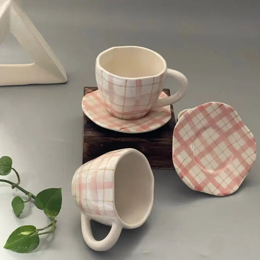 Set of Pink checkered ceramic mugs and coasters with pink and white checkered pattern on a gray surface.