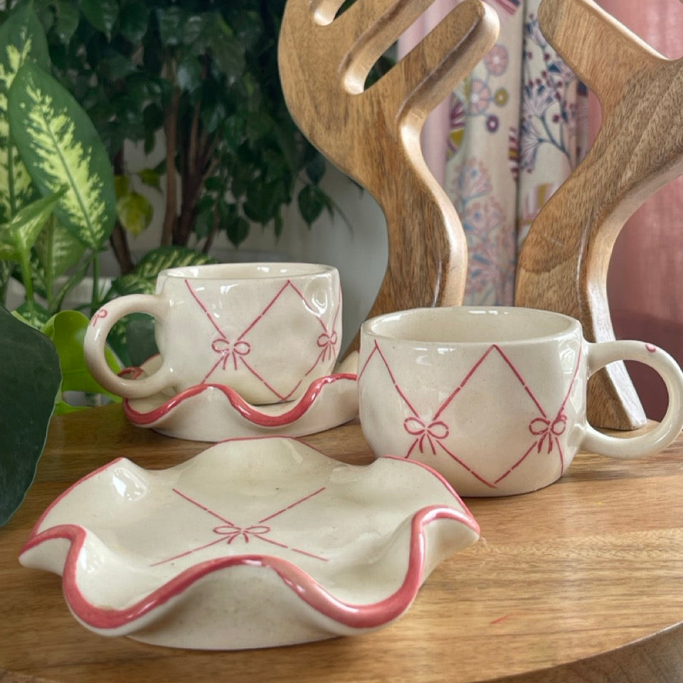 Two ceramic cups with decorative bow patterns on a wooden surface, accompanied by wooden utensils.
