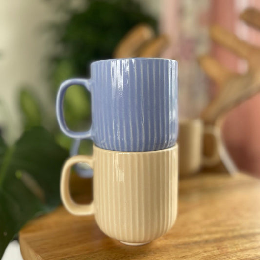 Two ceramic mugs (purple & beige) stacked on a wooden surface with a blurred background