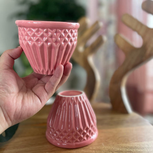Hand holding a pink textured ceramic cup bowl with another similar cup bowl on a wooden surface.