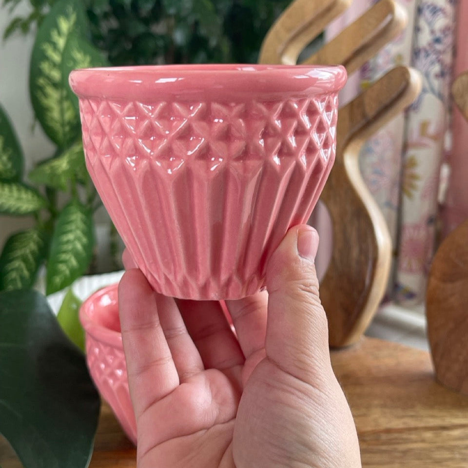 Hand holding a pink textured ceramic cup with a blurred background