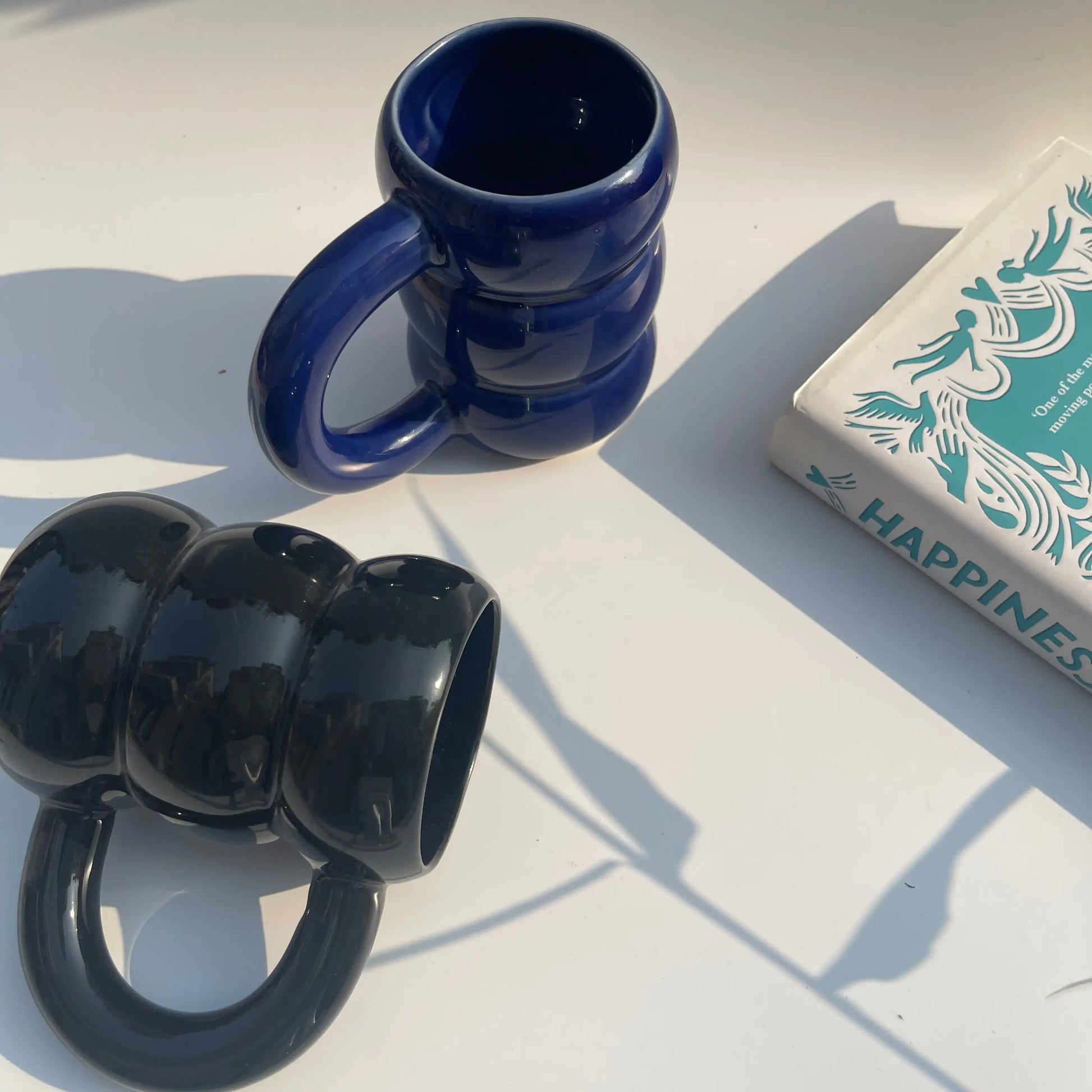 Twilight Duo Mugs on a white surface with a book titled 'Happiness' in the background.