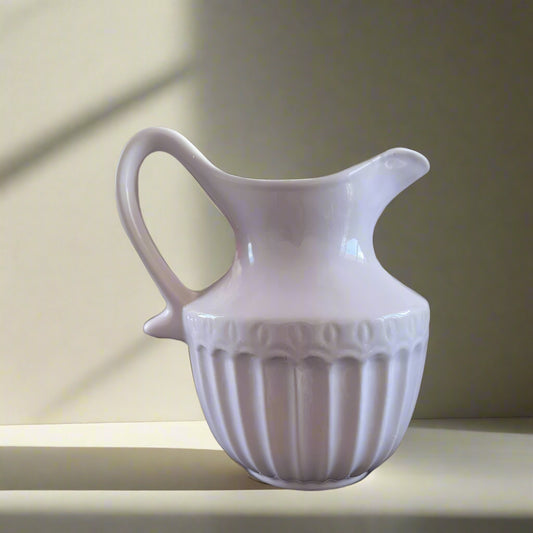 White ceramic pitcher with decorative patterns on a neutral background