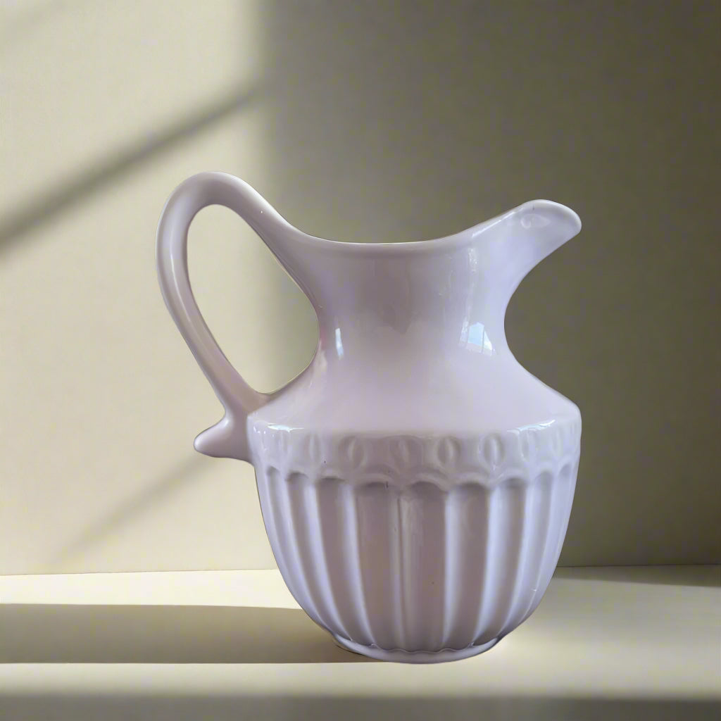White ceramic pitcher with decorative patterns on a neutral background
