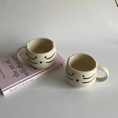 Two ceramic mugs with face designs on a book titled 'The Art of Self-Therapy'.